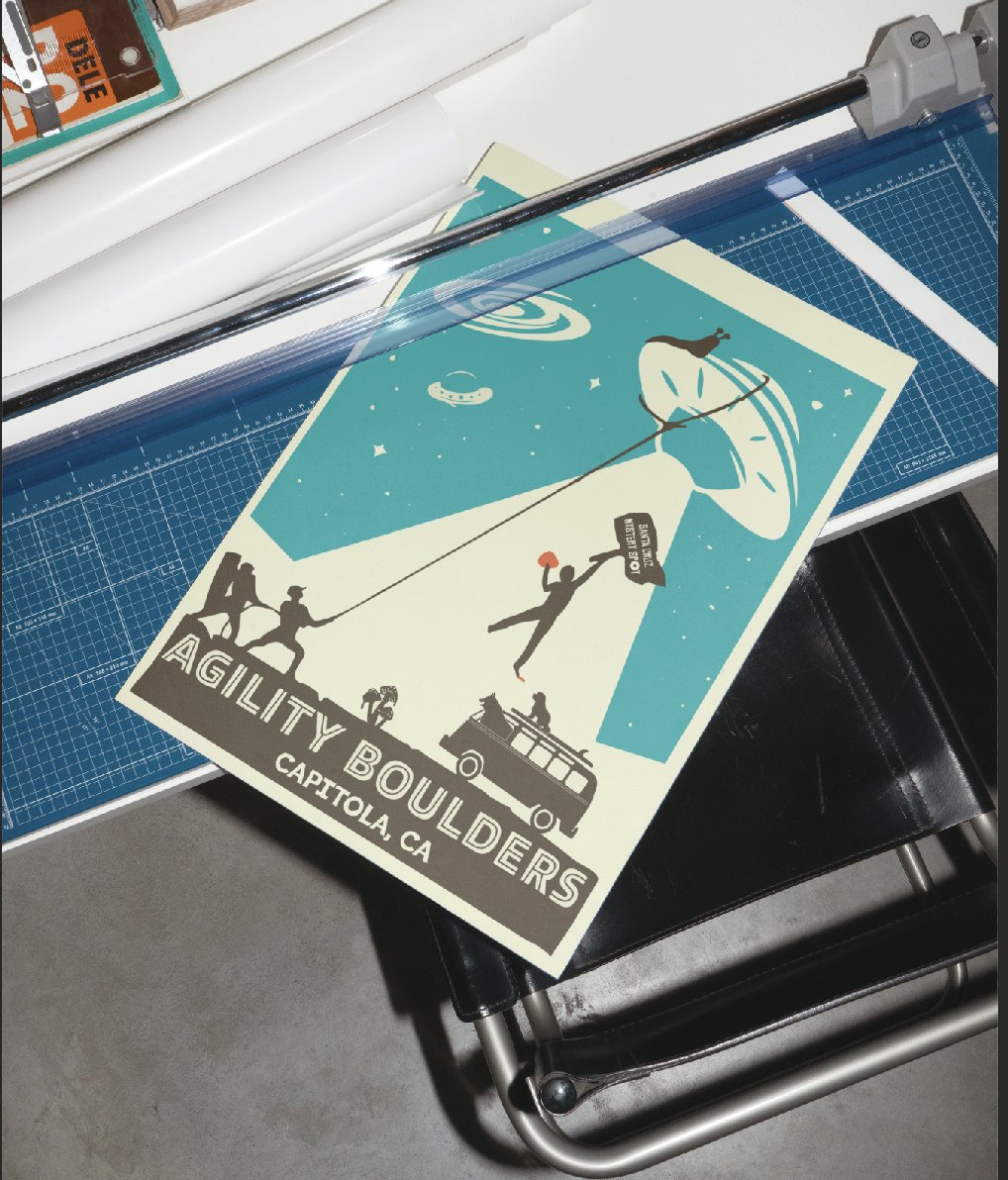 The UFO poster on a cutting mat under a guillotine trimmer, being cut down to size by hand.