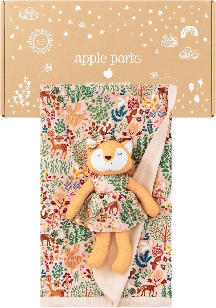An Apple Park kraft gift box printed with white stars, suns and rainbows, above a woodland-print blanket and a little fox plush.
