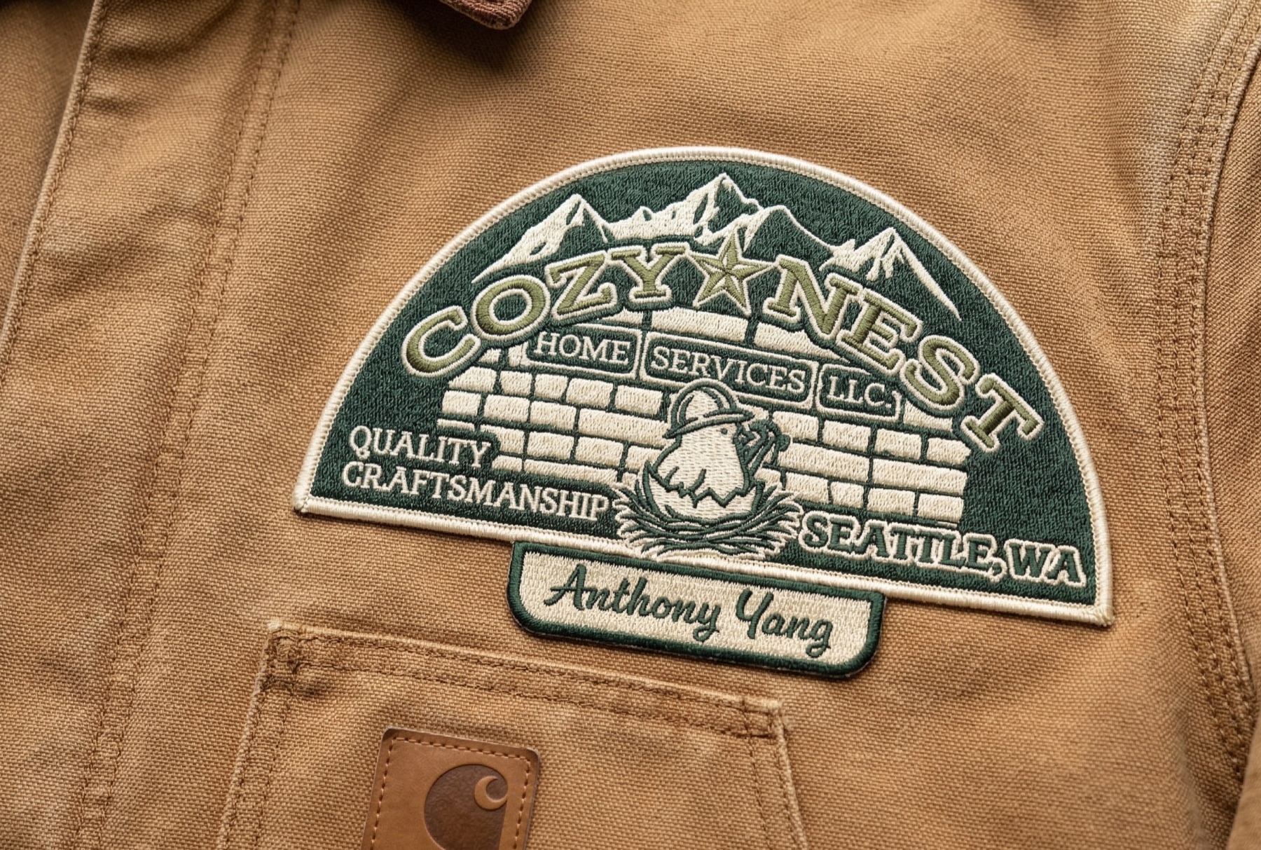 An embroidered Cozy Nest patch on a tan canvas work jacket, with a Quality Craftsmanship arch over the badge and an Anthony Yang name tape below it.