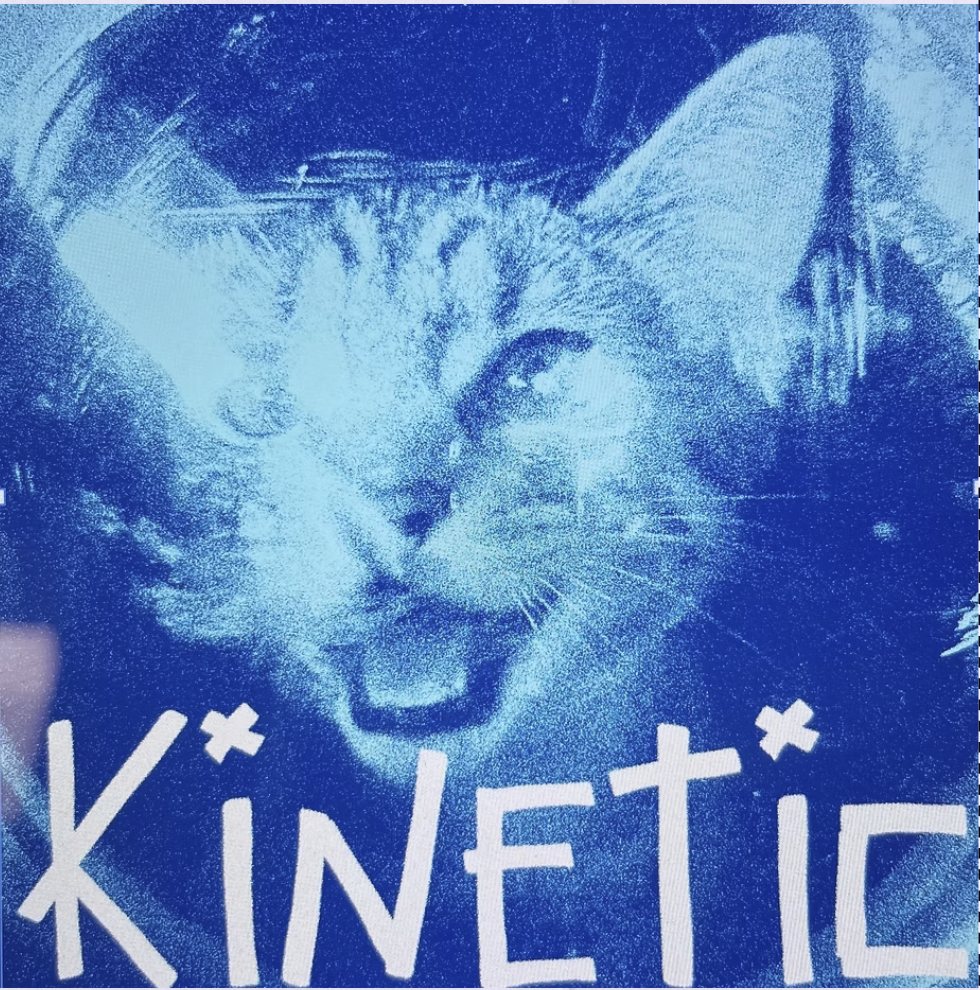 A cyanotype sticker in deep blue showing a cat with its mouth open, with KINETIC scratched across it in uneven white letters.