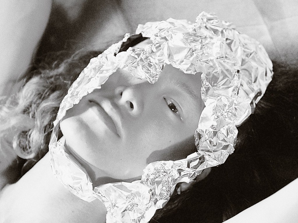 A face in black and white looking up from inside a crown of crumpled silver foil.