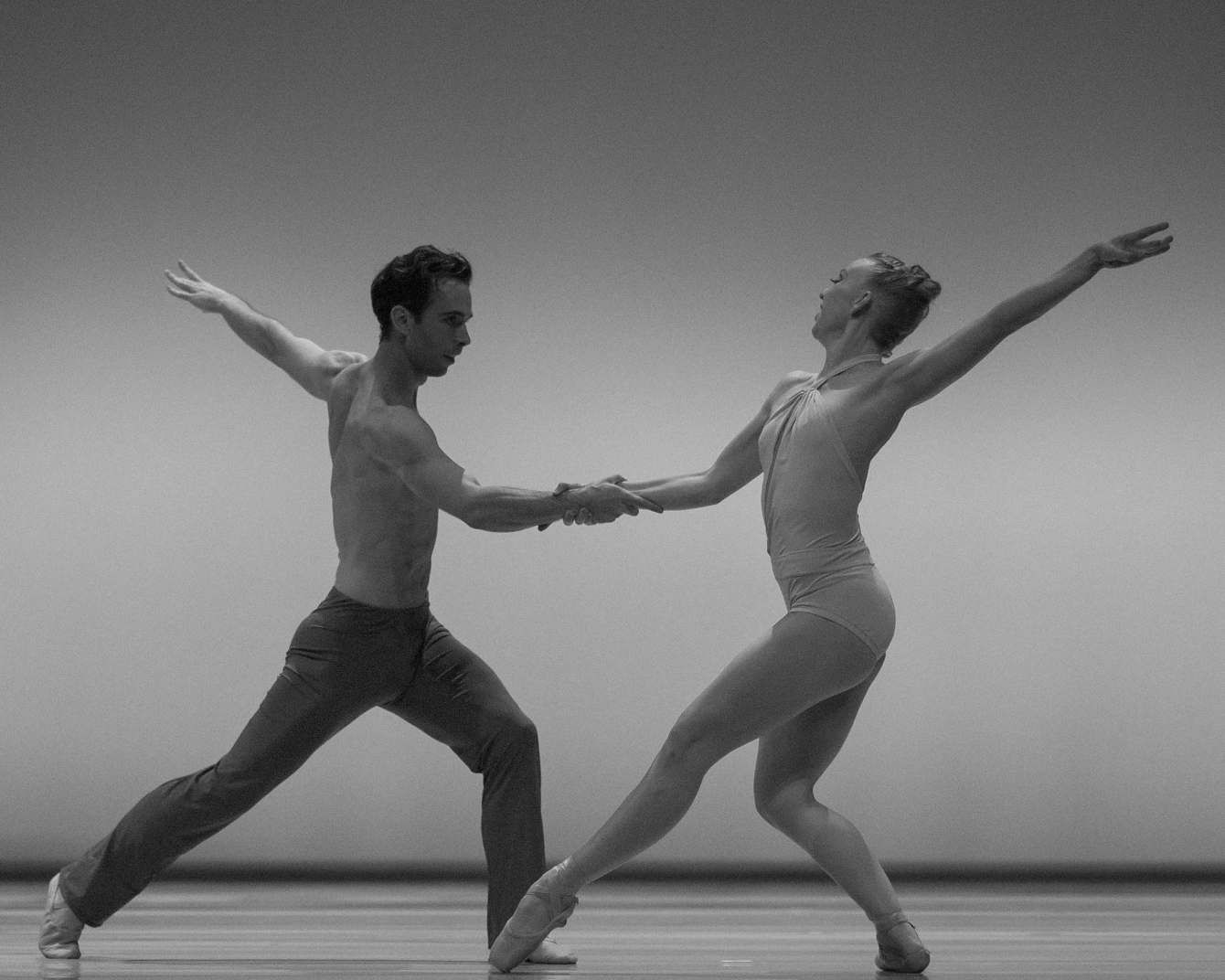 Two Smuin Ballet dancers in a deep lunge with hands joined, in black and white.