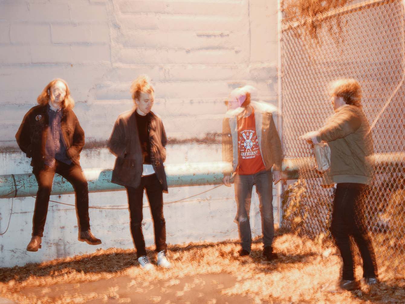 Four band members standing in a sunlit alley beside a chain-link fence, shot for Mad Sounds Magazine.