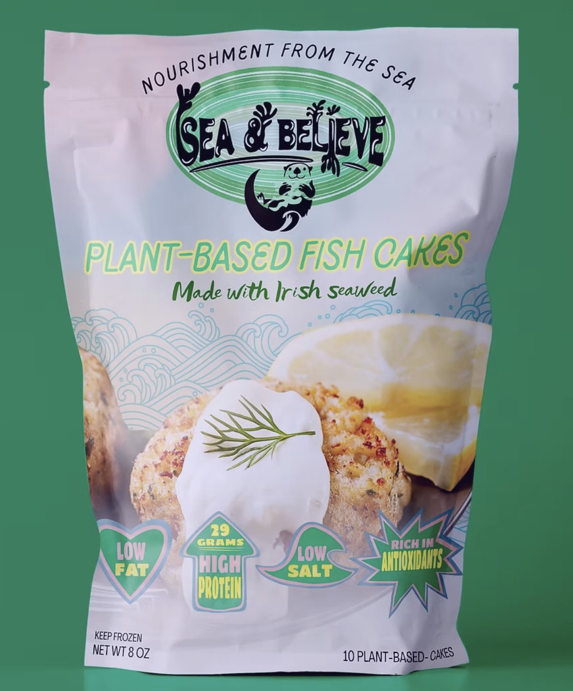 Sea & Believe plant-based fish cakes pouch on a pale ground, showing two golden fish cakes with a sprig of dill and a row of nutrition badges.
